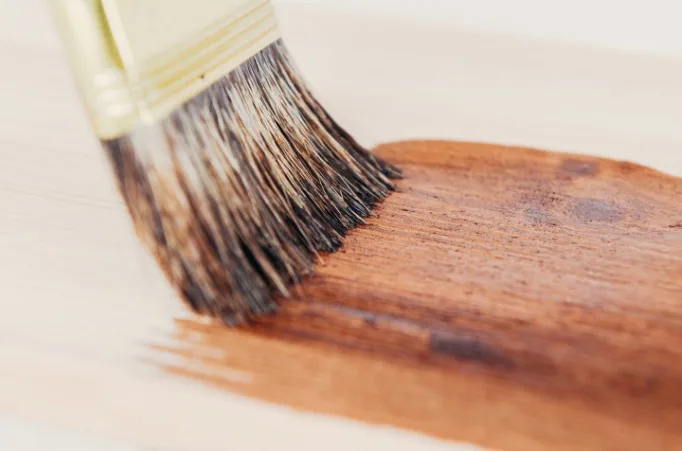 Primer plano de brocha aplicando tinte oscuro sobre tabla de madera clara en Burgos