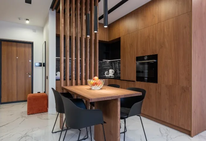 Cocina en L con isla-comedor, armarios en tono nogal oscuro, separador de listones de madera y sillas negras en Burgos