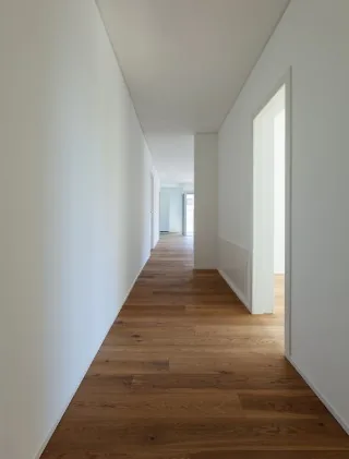 Pasillo largo de paredes blancas con suelo de tarima de madera oscura instalado, puerta blanca al fondo en Burgos