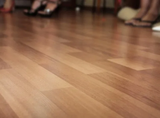 Primer plano de suelo de madera clara barnizada con pies en chanclas desenfocados al fondo en Burgos