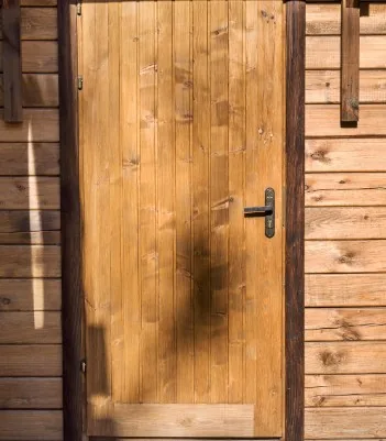 Puerta rústica de madera de pino en cabaña de troncos con manilla negra en Burgos
