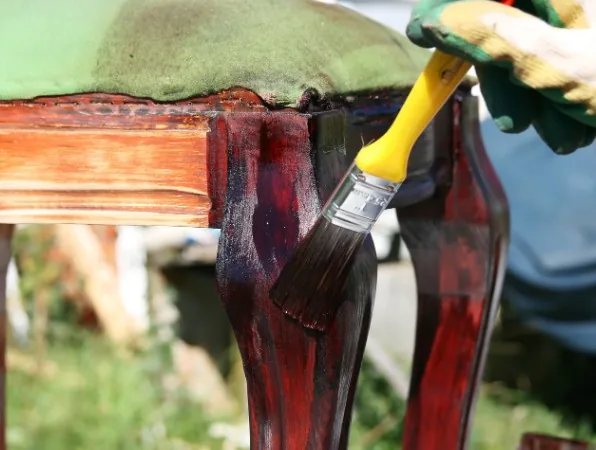 Restauración de pata de silla/taburete con tapizado verde, aplicando tinte rojo oscuro con brocha en Burgos