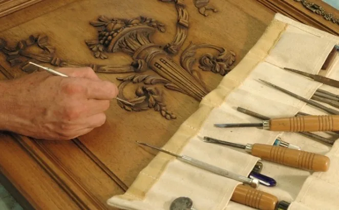 Restaurador tallando a mano un panel de madera con relieve ornamental de frutas, herramientas de talla en estuche en Burgos