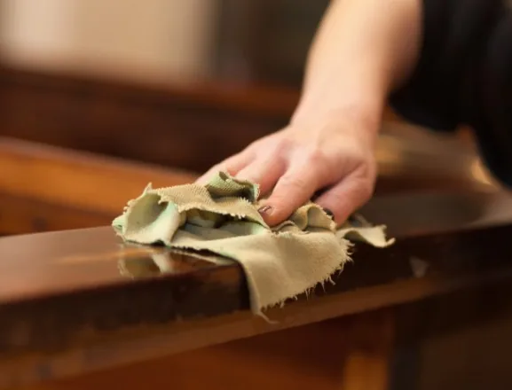 Mano puliendo con paño un mueble antiguo de madera oscura barnizada en Burgos