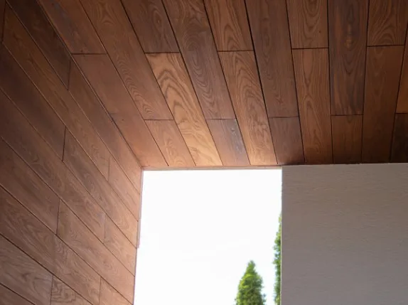 Techo y esquina revestidos con lamas de madera oscura en porche exterior, vista hacia el jardín en Burgos