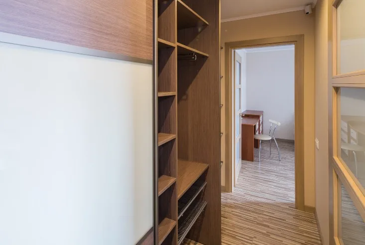Detalle de armario corredero con panel blanco y estantería interior de madera junto a pasillo en Burgos