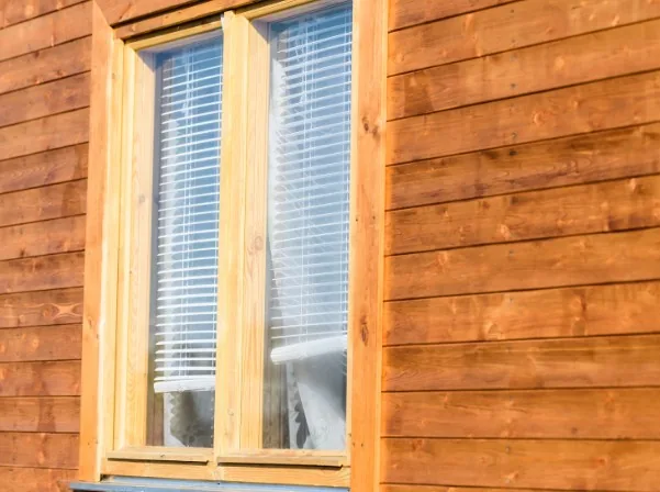 Ventana de madera clara en fachada de cabaña con estores blancos en Burgos